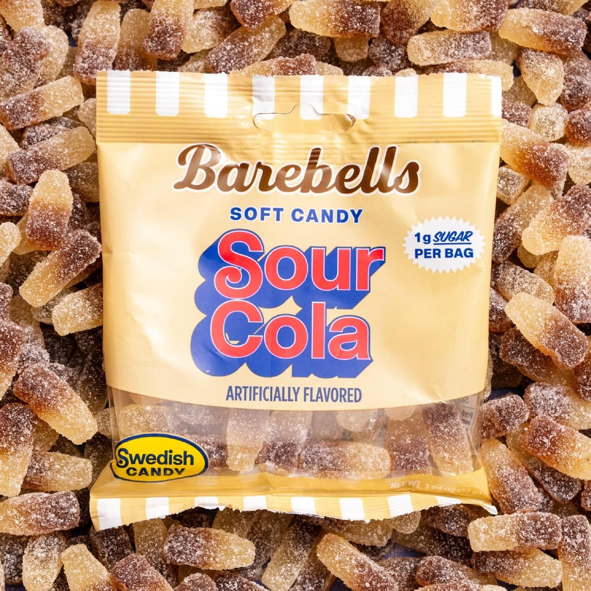 Barebells Soft Candy Sour Cola gummy bag on a pile of sugar-coated cola bottle candies