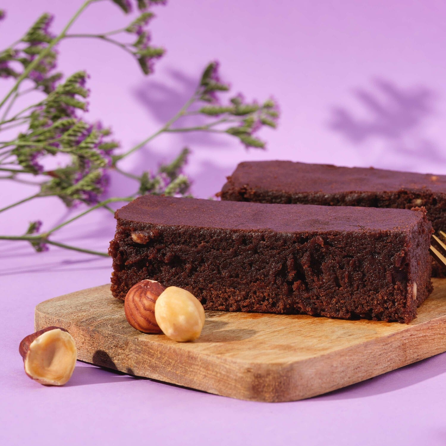 Prozis Protein Brownie slice on a wood board with hazelnuts and flowers