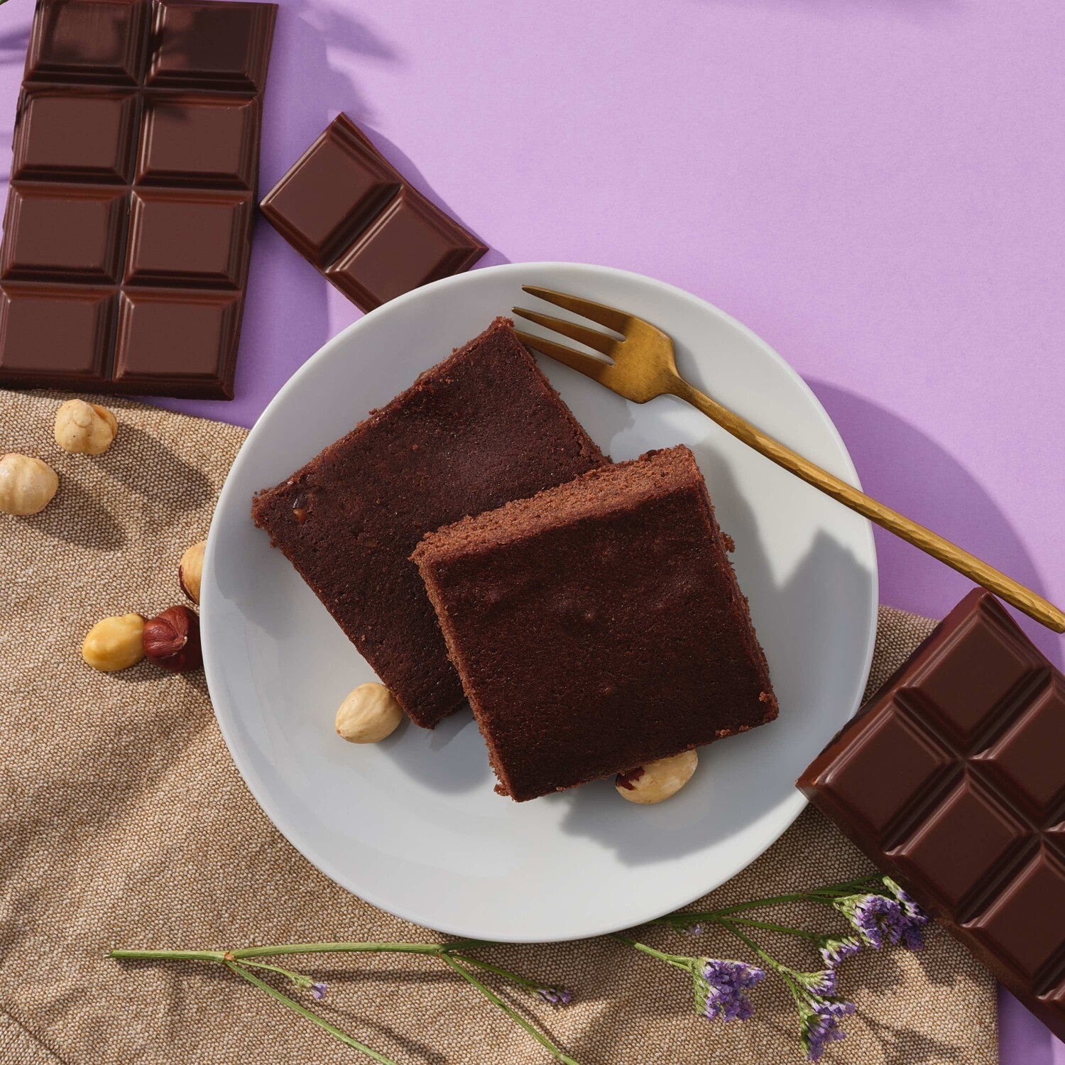 Prozis Protein Brownie squares plated with dark chocolate bars and hazelnuts
