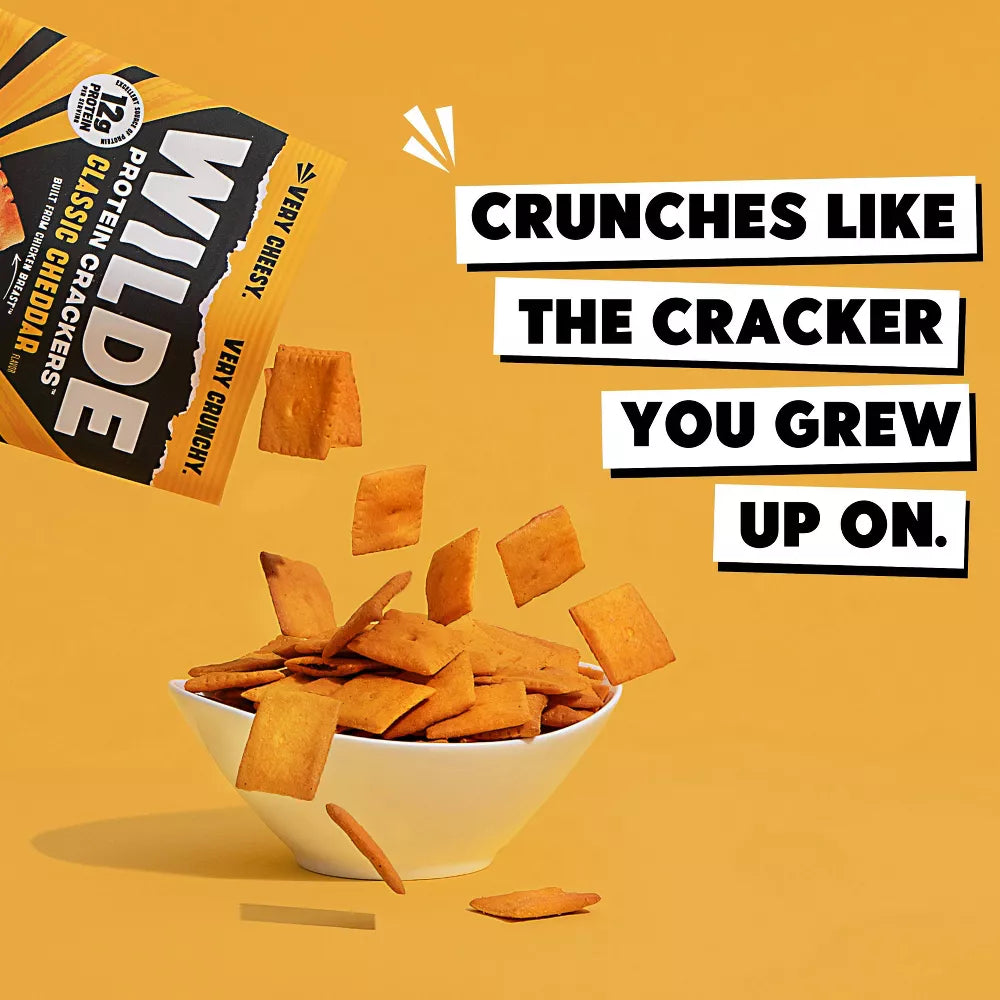 Wilde Classic Cheddar Protein Crackers poured into a white bowl, cheesy square high-protein snack