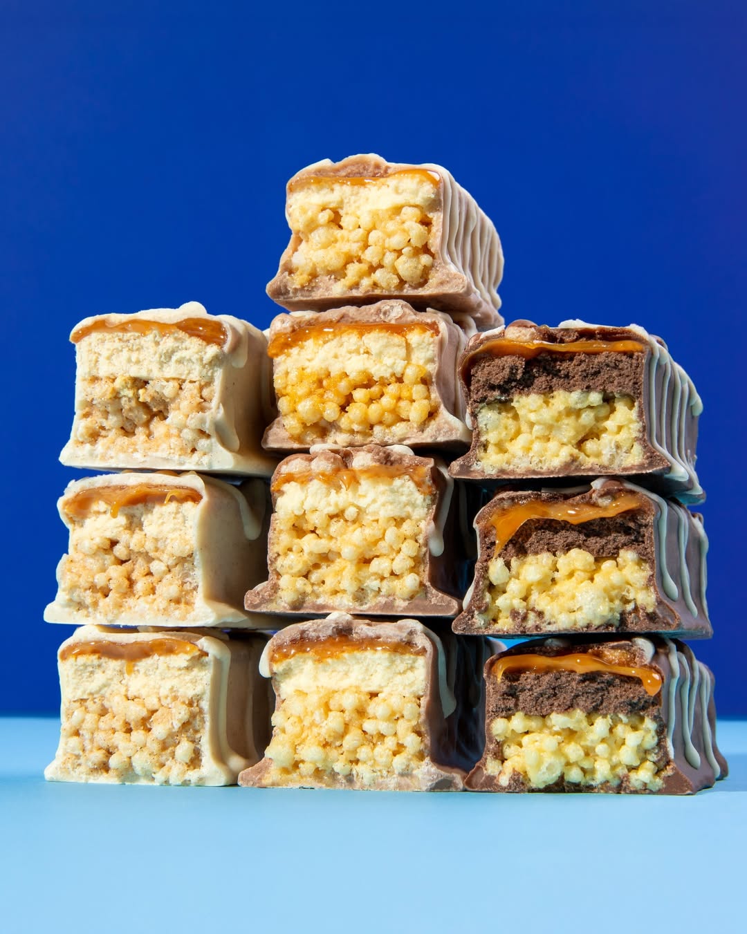 Quest Nutrition Stacks protein bars stacked in a pyramid on blue showing crispy caramel and chocolate layers
